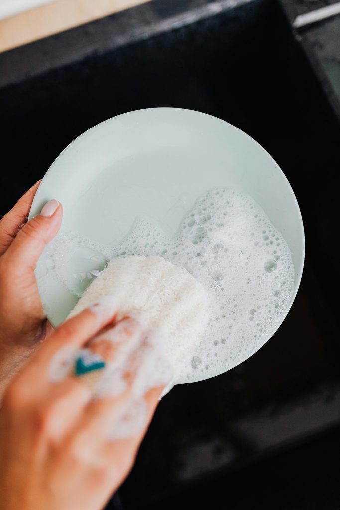 Hands washing a green plate with soap and water in the kitchen sink.