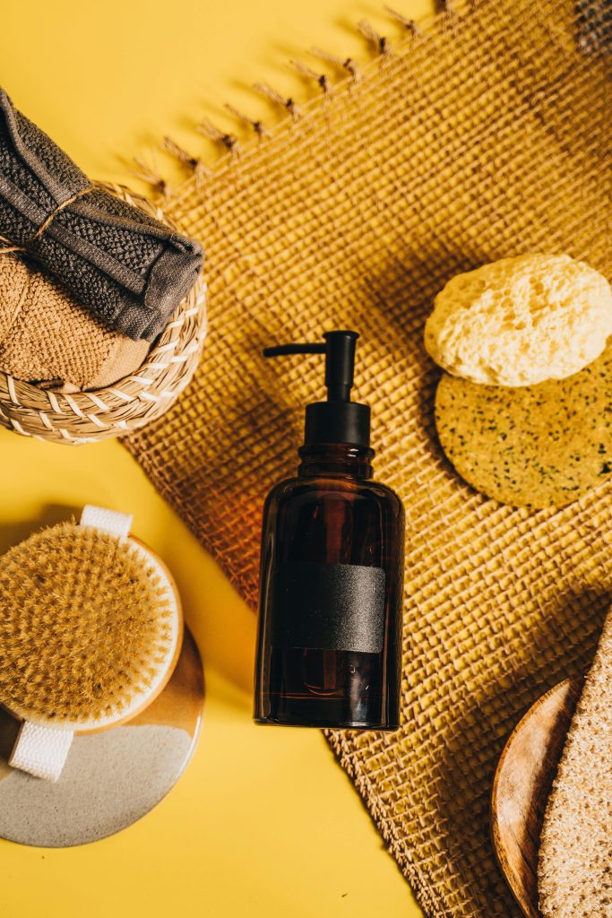 Flat lay of spa essentials including a pump bottle and exfoliating brushes on a woven mat.