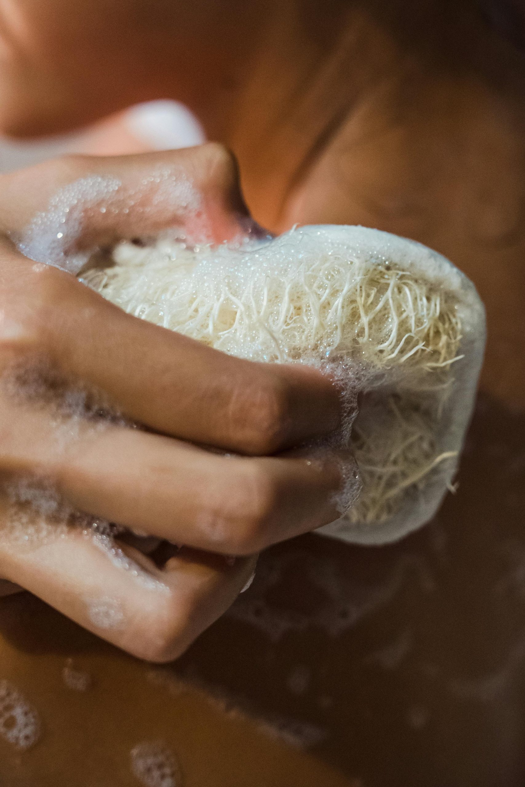 Close-up of a person using a loofah for skin exfoliation with soap suds.
