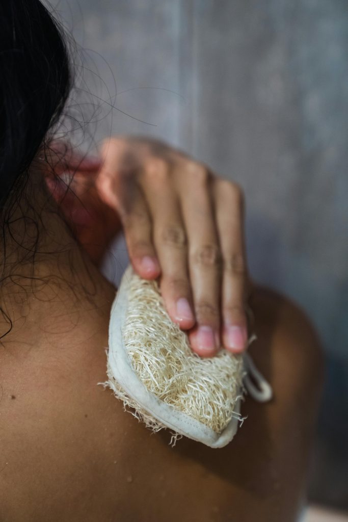 Close-up of a person using a loofah for skin exfoliation in the shower.